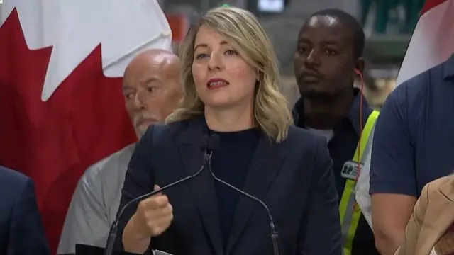Melanie Joly speaking at a podium in front of Canadian flag