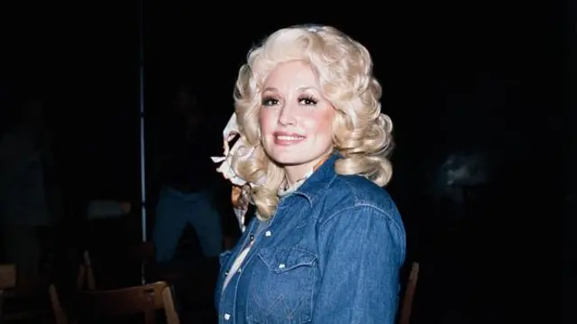 Parton in a denim jacket and blonde curly styled hair