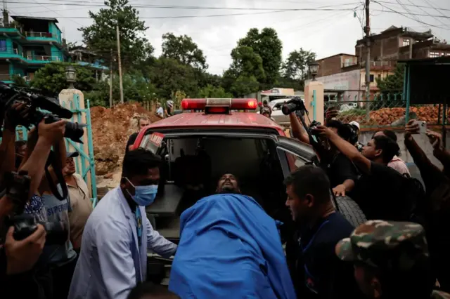 An injured man covered in a blue blanket is loaded into an ambulance.