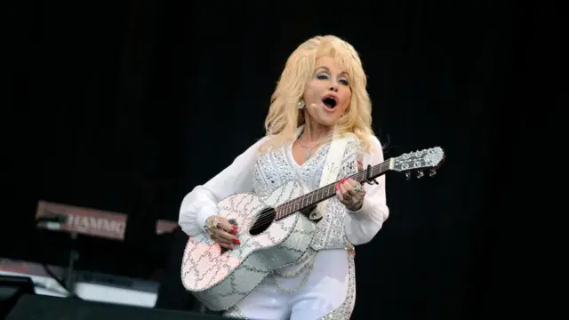 Dolly Parton signs and holds a pearly white guitar which matches her outfit during a performance
