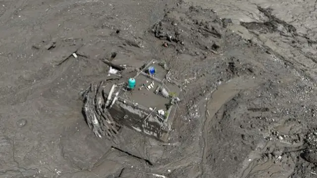 A house entirely covered in mud, with just the roof and front wall visible