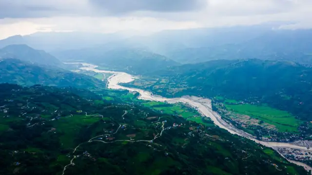 Bhotekoshi River in Nepal, with flooding visible on either side of the banks. Lush green fields are seen on the hills.