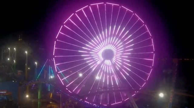 A ferris wheel lit up pink with white hearts in the middle