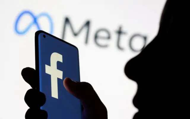 The Facebook logo displayed on a phone with the Meta logo visible on a screen behind it