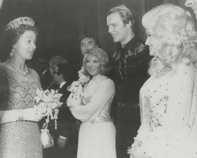 Queen Elizabeth II and Dolly Parton meeting each other, in a black and white photograph