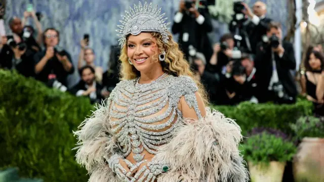 A woman in a flamboyant feather and diamante outfit with a bank of photographers in the background