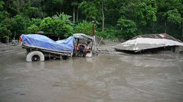 A truck and house partially submerged in water and mud
