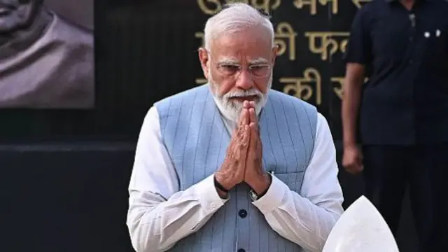 Narendra Modi is pictured with his hands clasped in a prayer motion, and head slightly bowed.