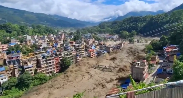 Floodwaters coursing down a river through a town, a bridge is being carried by the water