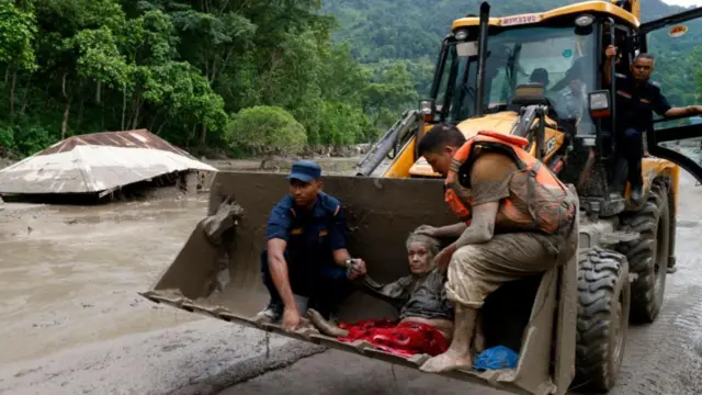 Rescuers transport an older woman following a flash flood in Trishuli Bazar, Nuwakot district