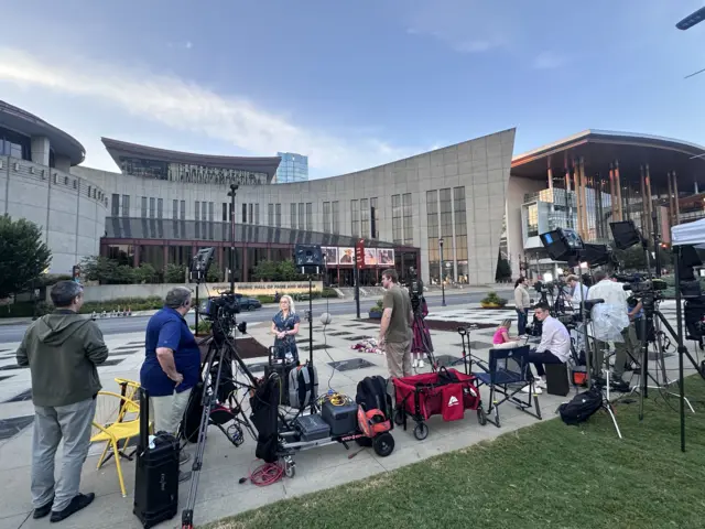Camera crews sat and stood outside a large building