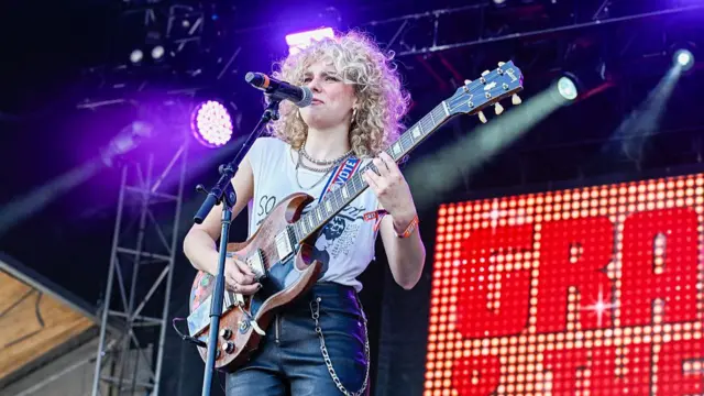 Bowers plays guitar and sings into a mic