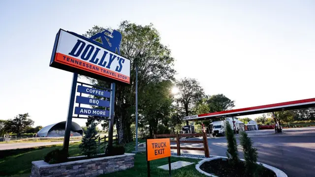 A sign that says Dolly's Tennessean travel stop and a petrol forecourt with a lorry parked in it