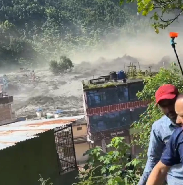 A screenshot of a video showing people climbing a hiil as floods engulf a village
