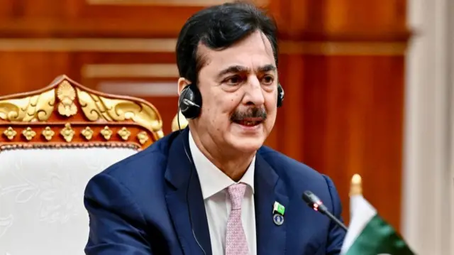 Syed Yousaf Raza Gilani is speaking during a meeting at the Senate in Phnom Penh, Cambodia. He has jet black hair and a mustache and is wearing a blue suit with a white shirt and pink tie