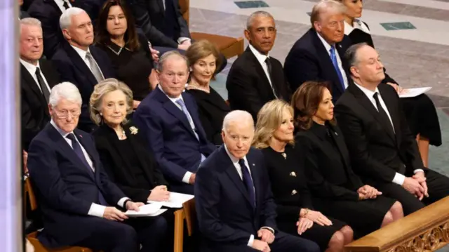 Men and women in dark suits sit in pews