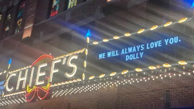 A sign on a bar which says we will always love you dolly