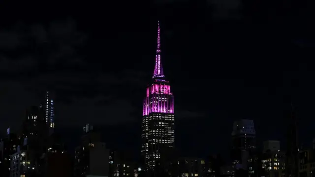The top of the Empire State Building is lit up pink and glows against a dark New York skyline