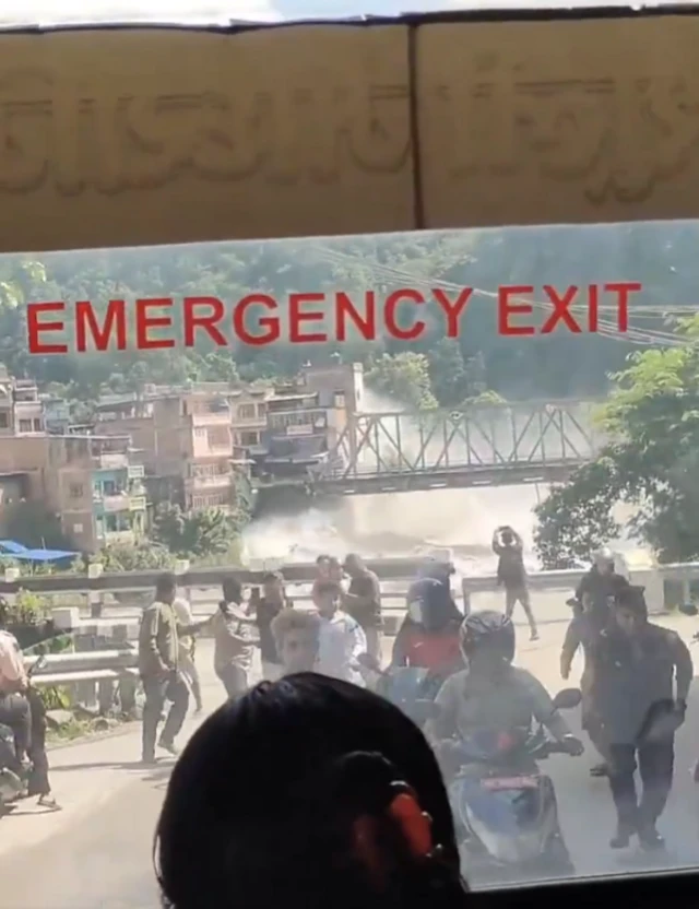 A screengrab from a video filmed inside bus. Floodwaters rushing down under a bridge, around a dozen people can be seen behind fleeing on foot or moped.