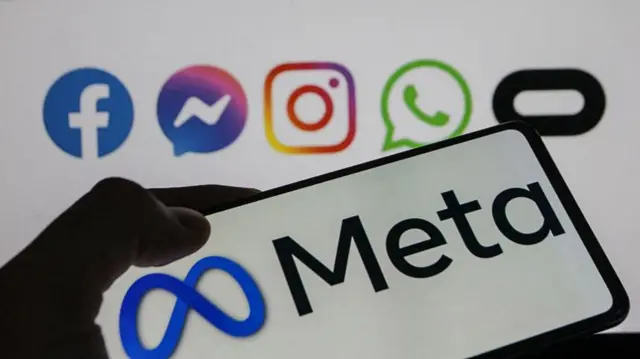 The Meta logo on a phone and the logos of its various platforms on a screen in the background