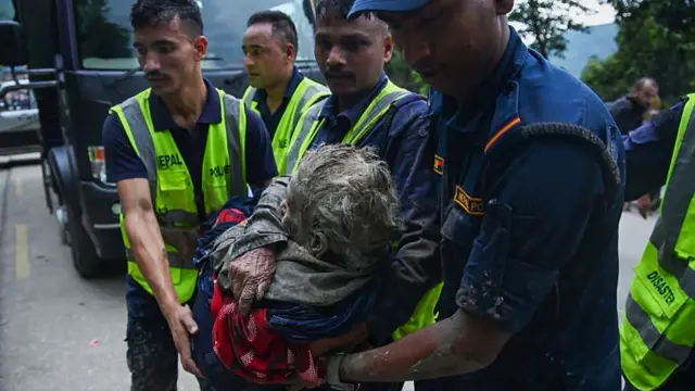 Rescue workers carry an older woman who is covered in mud and wrapped in a blanket.