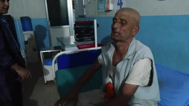 Keshav Prasad Baral sits on a blue hospital bed. His eyes are closed and his head is shaved.