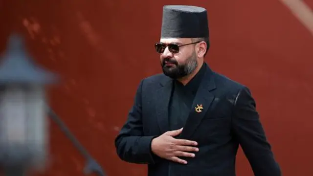 Balen Shah wears a black suit and had and walks towards a microphone