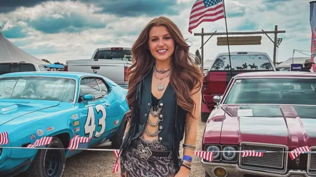 Taynee Lord smiling in a field in front of cars adorned with US flags