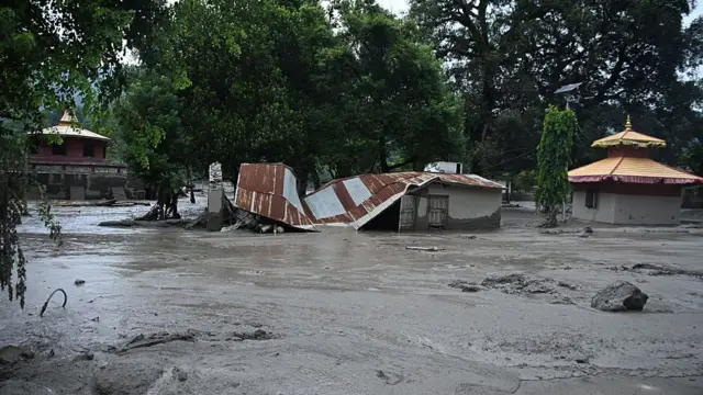 A house with a collapsed roof is submerged in mud and debris in the middle of a residential area in Nepal's Nuwakot district