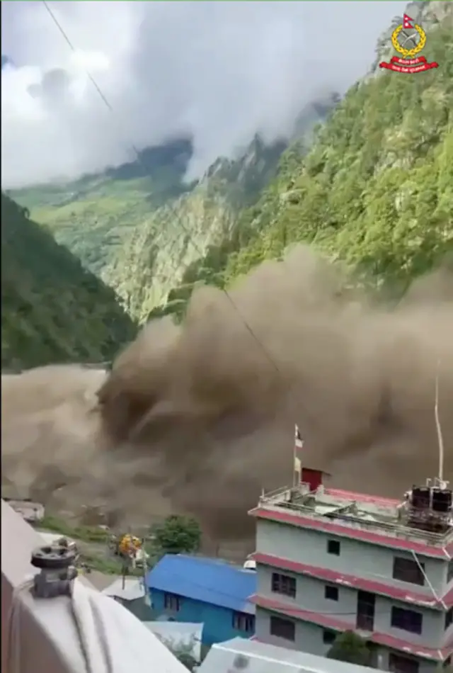 A huge wall of brown water behind two buildings