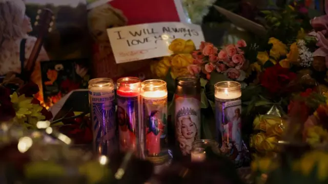 Candles lined up in front of flowers and a written poster that says i will always love you