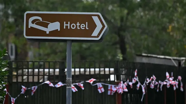 A hotel sign in front of a fence with English flags