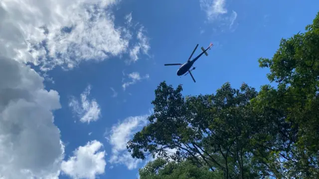 A helicopter is pictured from the ground as it flies overhead above some trees