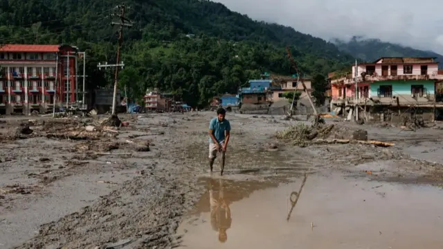 A man lifts his trousers as he wades through the mud that covers the road