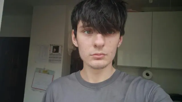 Tyler looking at the camera with a blank facial expression, with his fringe above his eyes