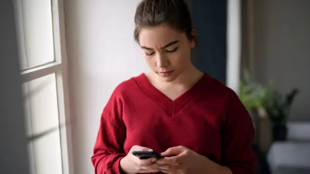 A disappointed-looking young woman looking at her phone.