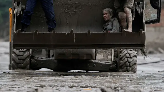 Elderly woman covered in mud, evacuated from the site of massive mudslide in Nepal on board an excavator