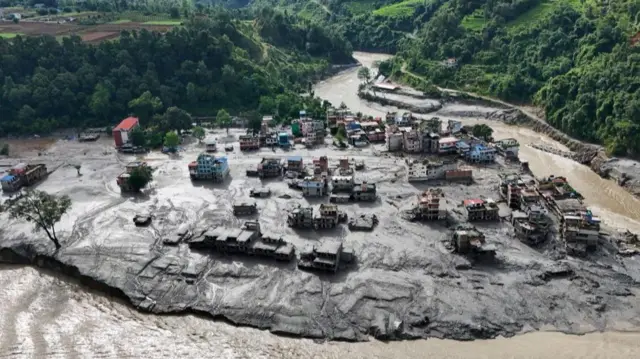 A drone view showing mud covering buildings while the river runs around the residential area