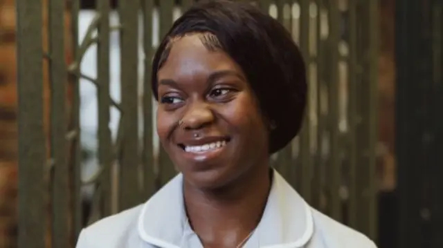 Asia Mason at her workplace, smiling, looking away from the camera, wearing her scrubs