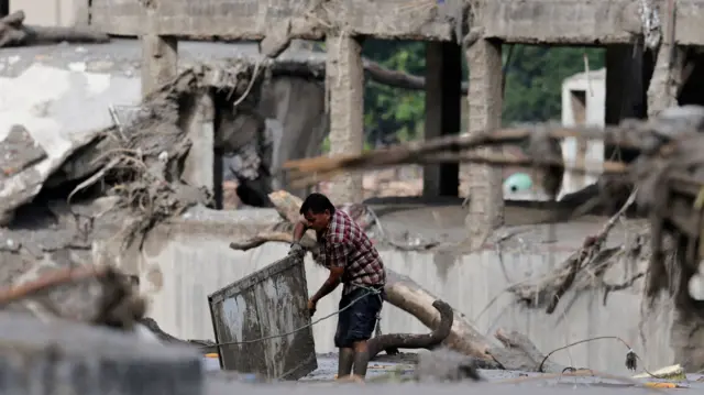 A man lifts a panel out of the mud as he is surrounded by destroyed buildings