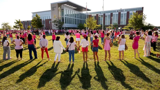 hundreds of women in pink gather outside a courthouse, with many forming a circle by holding their hands