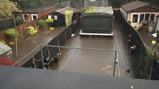 Three gardens, completely flooded with water showing high up the fences