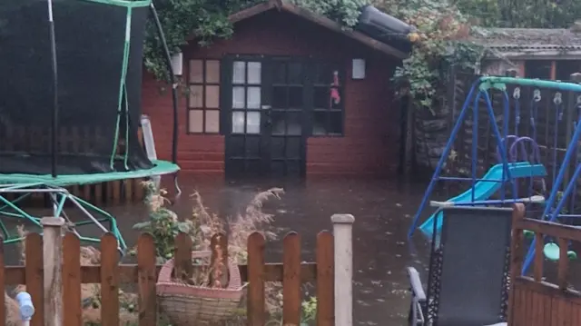 A flooded gardens with a shed swing and trampoline