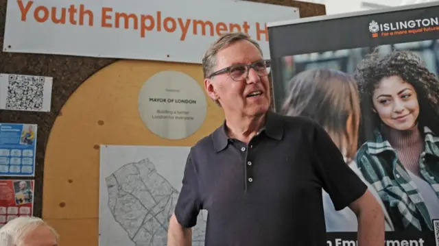 An older man in a dark polo shirt and glasses.
