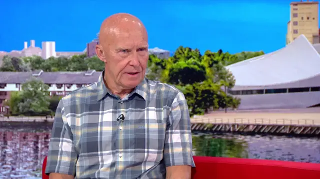 Alan Hinkes is wearing a grey and white checked shirt while sitting on a red sofa in the BBC Breakfast studio