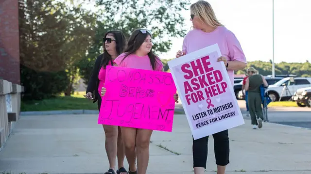 three women in pink walking outside courthouse, with two holding signs that read "She asked for help, listen to mothers, peace for Lindsay" and "compassion before judgement"