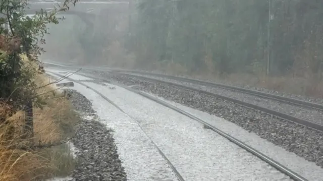 A railway line, which curves around the corner to the left under a bridge, between two lines of trees, has been flooded by heavy rain.