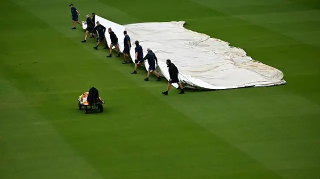 Ground staff drag the covers on the pitch