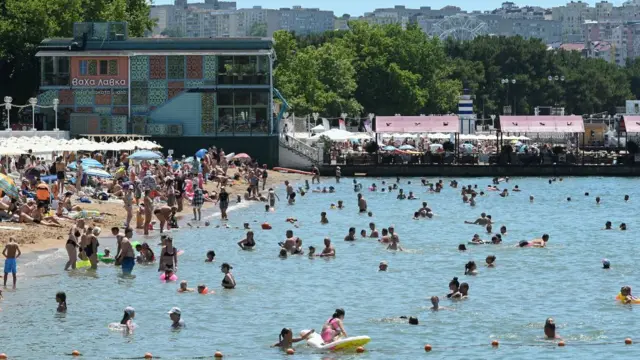 A crowded beach on a sunny day, with seaside restaurants in the background