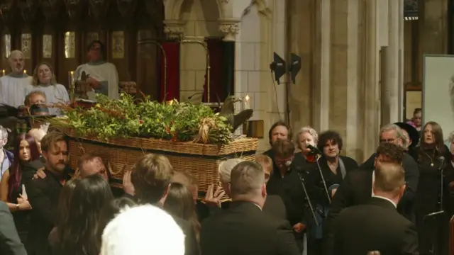 Closeup of the wicker coffin being carried